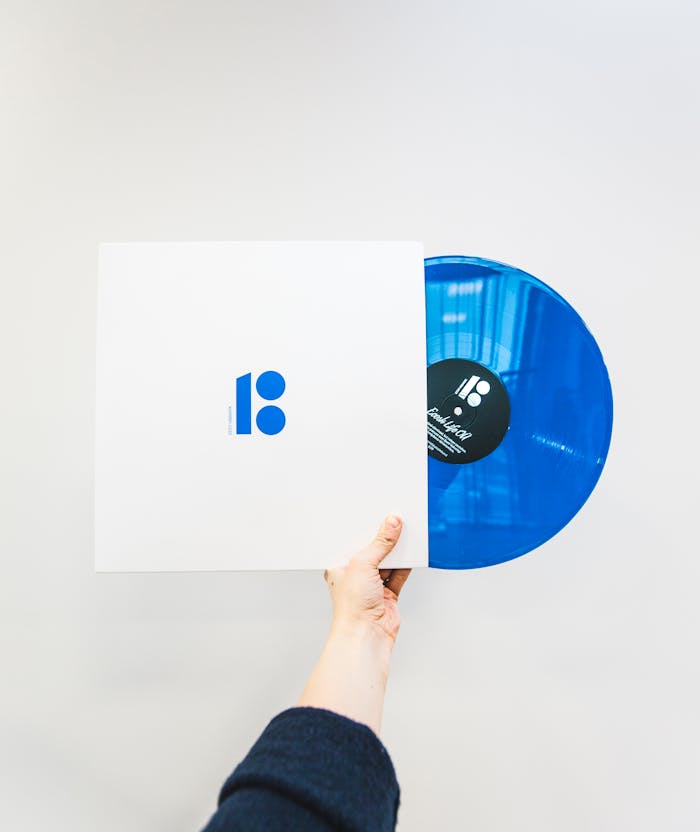 A hand holding a blue vinyl record partially out of its sleeve, depicting music and vintage aesthetics.